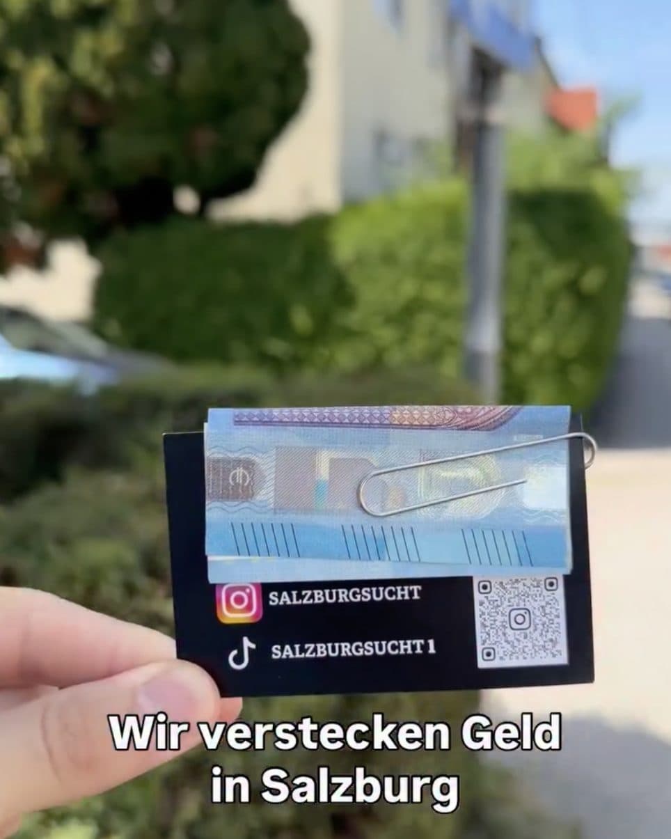 Eine Hand hält eine Karte mit angeklammertem Geldschein vor eine Hecke
